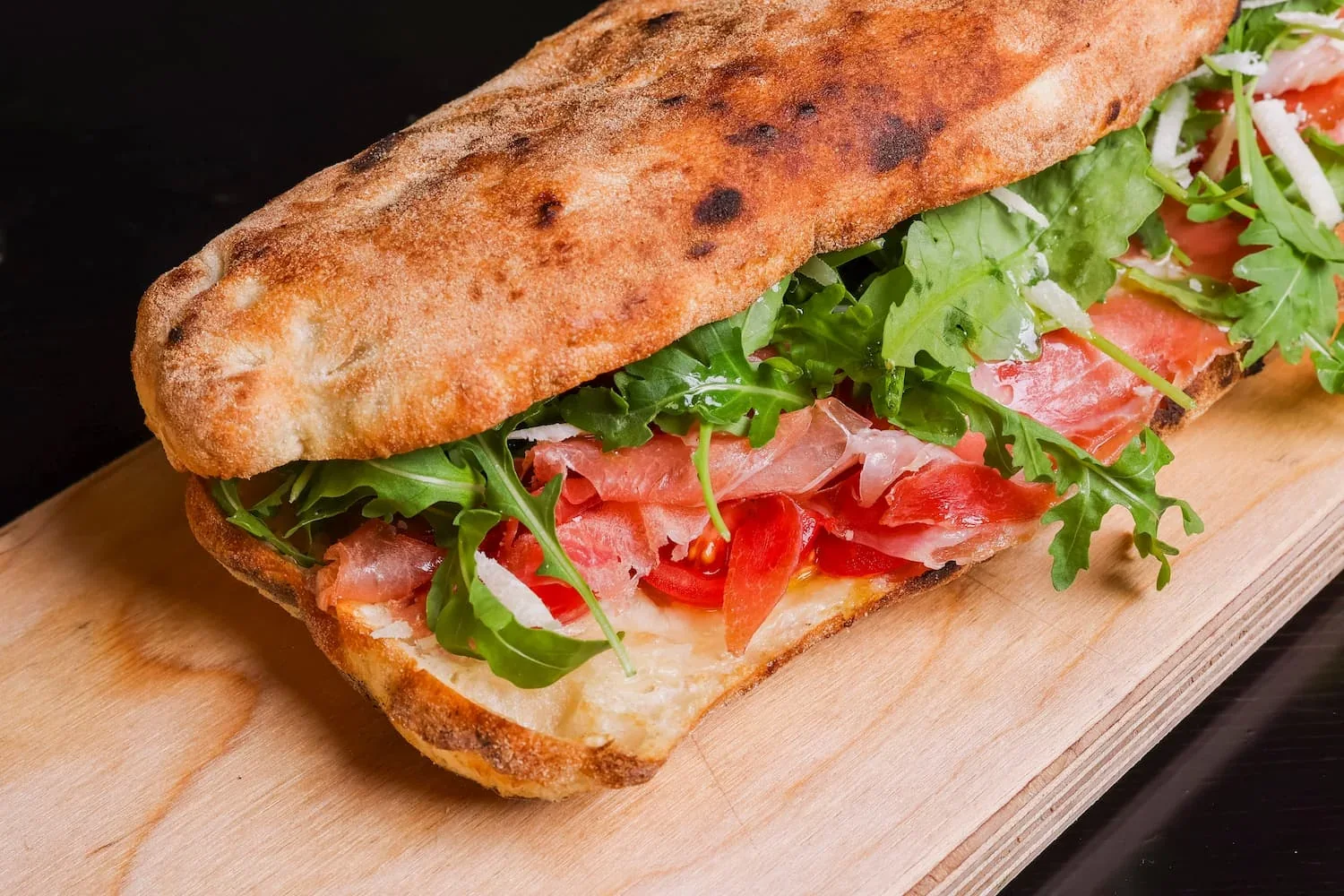 Un panuozzo coupé en deux, garni de jambon cru, de roquette, de tomate et de copeaux de fromage