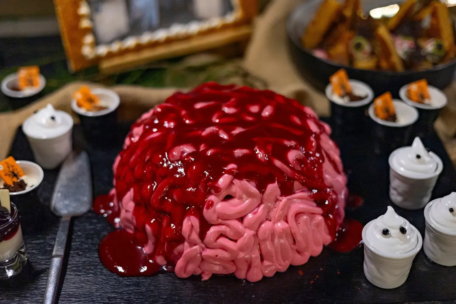 Un gâteau en forme de cerveau nappé d’un glaçage rouge, entouré de petites meringues fantômes