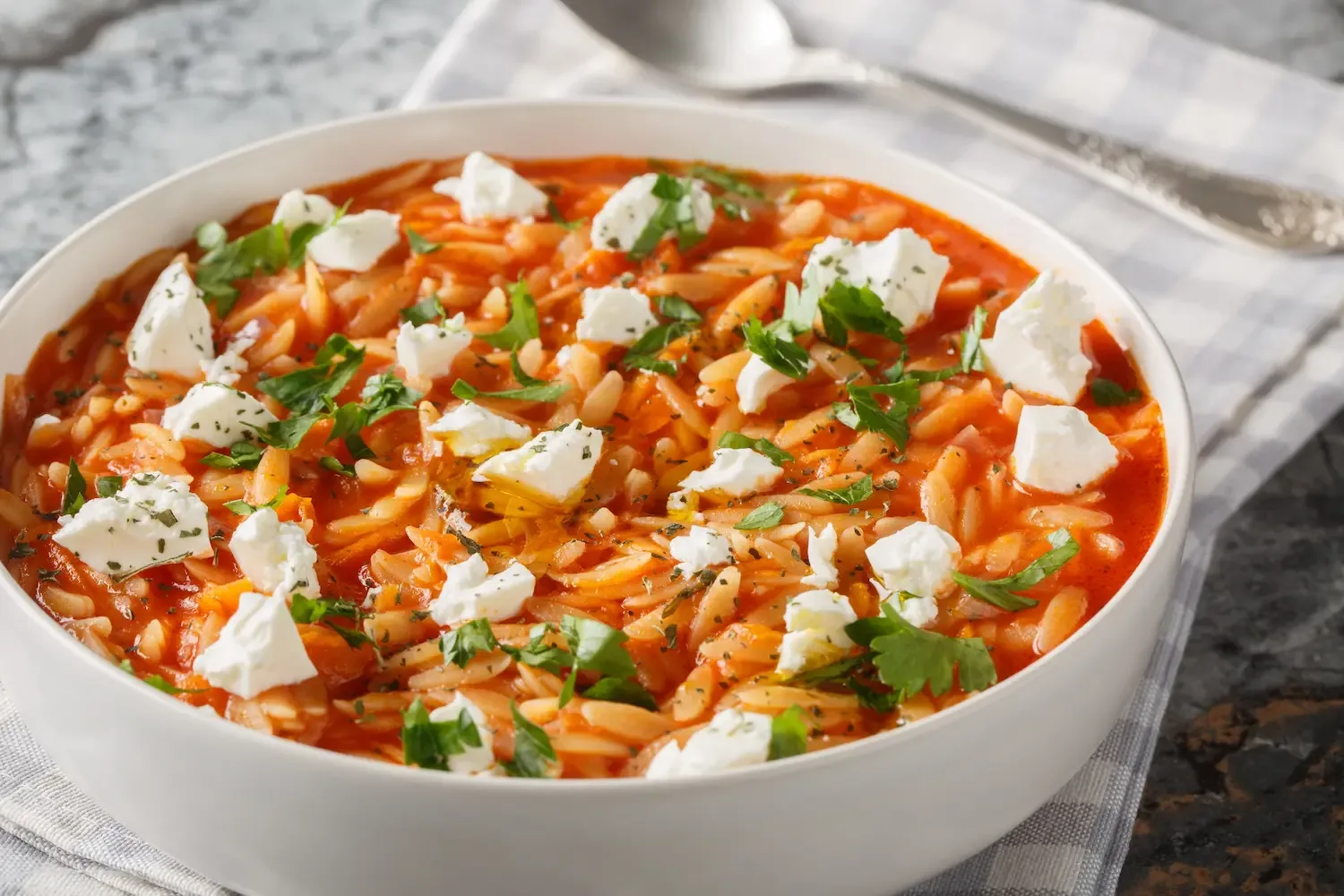 Un plat d’orzo nappé de sauce tomate, garni de cubes de feta et de persil frais.
