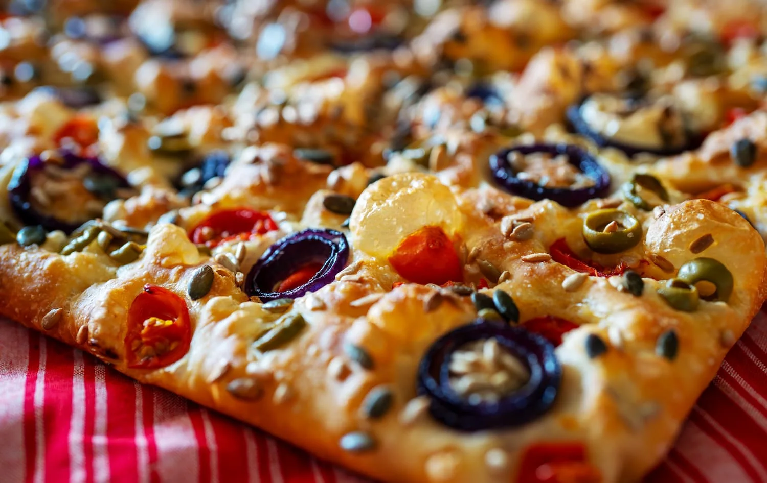 Une focaccia dorée en gros plan, garnie d’olives, de tomates et de graines