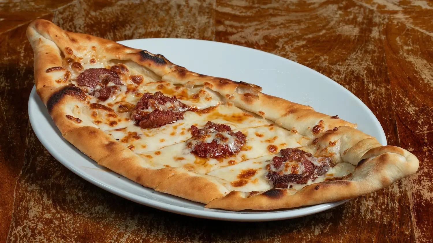 Une pide turque en forme de barque, dorée, garnie de viande épicée et de fromage fondu