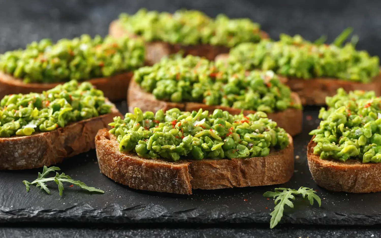 Des tartines de pain de campagne garnies de petits pois écrasés, avec de la roquette fraîche.